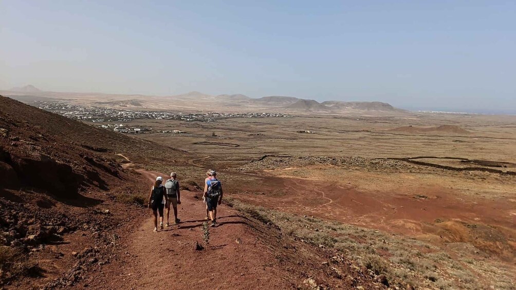 A group of hikers on a dirt trail with a view of a distant town and mountains. 3