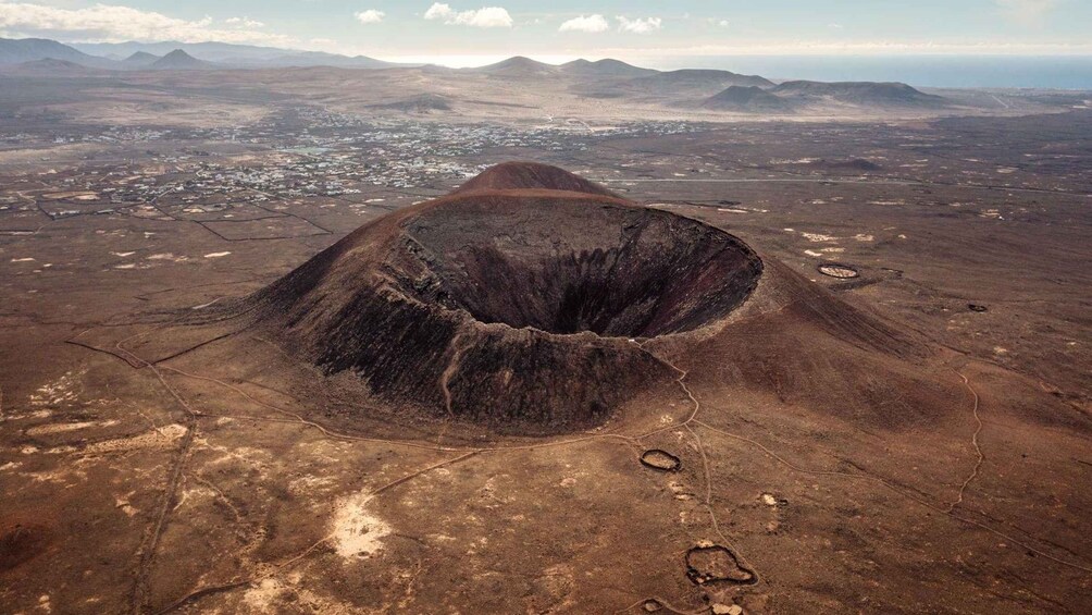 A large volcanic crater surrounded by a barren landscape with distant mountains and a small settlement. 2