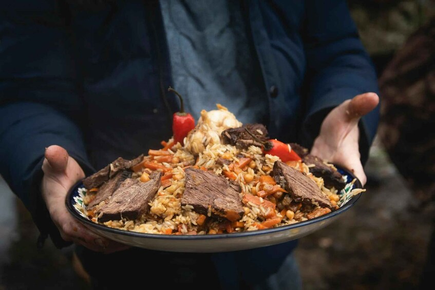 A person holding a plate of food with rice, meat, and vegetables. 2