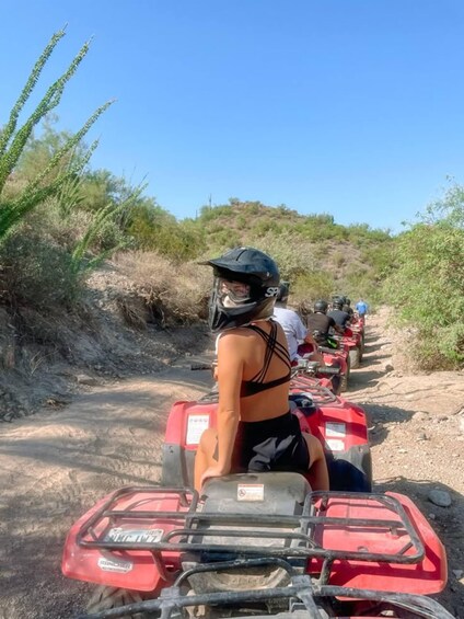 A group of people on red ATVs on a dirt path surrounded by vegetation. 2