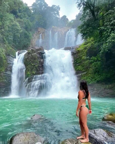 A waterfall cascading into a turquoise pool surrounded by lush greenery. 1