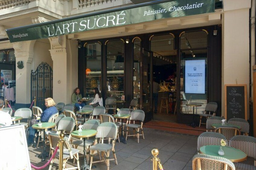 An outdoor cafe with wicker chairs and tables, a storefront with a sign reading 'L'ART SUCRE,' and a chalkboard menu. 5