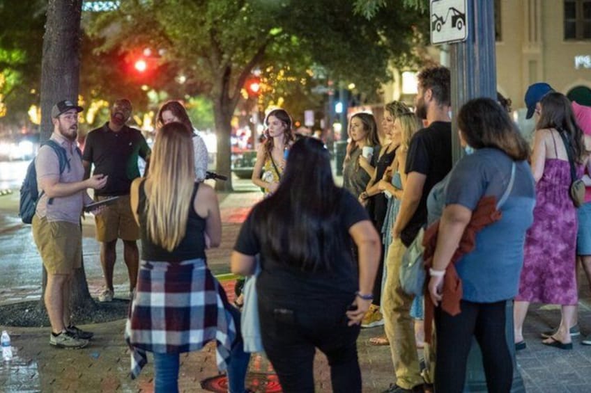 A group of people standing on a sidewalk at night, engaged in conversation. 5
