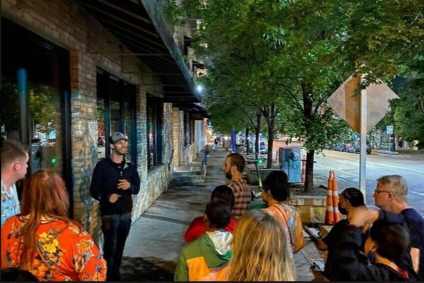 A group of people gathered on a sidewalk at night, with buildings and trees in the background. 4