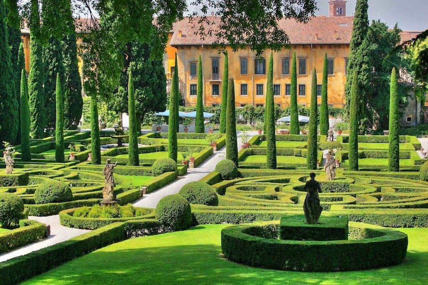 A formal garden with manicured hedges, statues, and a classical building in the background. 1