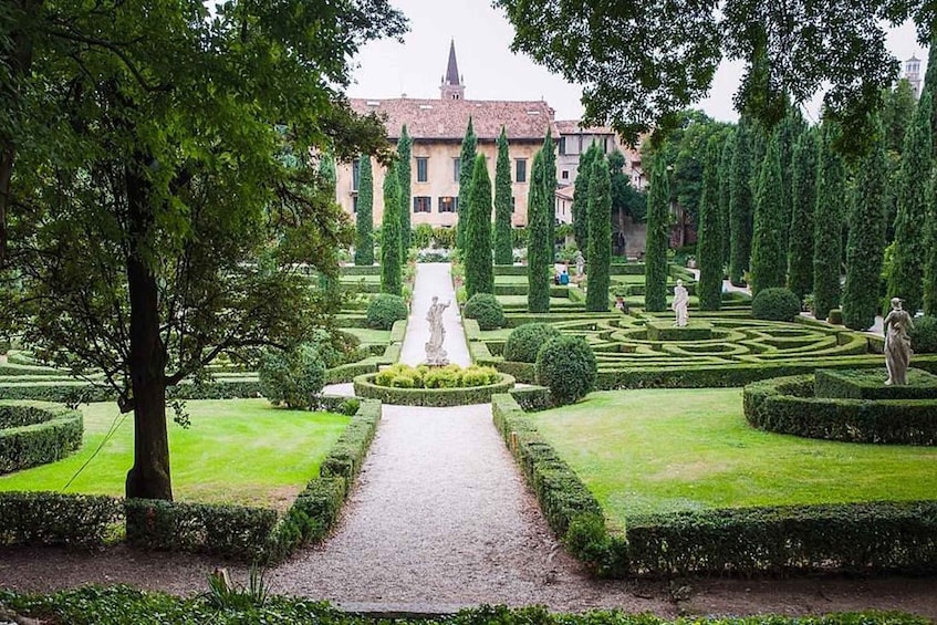 A formal garden with a central pathway, trimmed hedges, and statues. 2