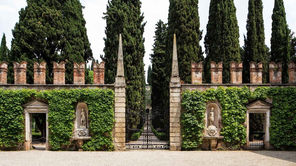 A historic building with tall cypress trees, a wrought iron gate, and statues. 3