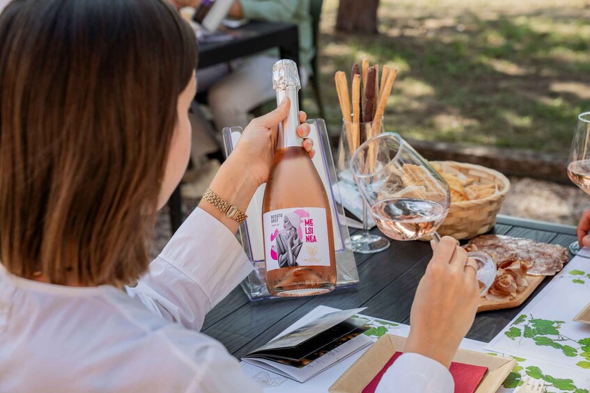 A person holding a bottle of rosato brut wine, a glass of wine, and a basket of breadsticks. 5