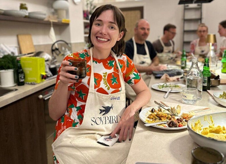 A person holding a glass of beverage, wearing an apron with a tomato pattern and the word 'SOVBIRD' on it. 5
