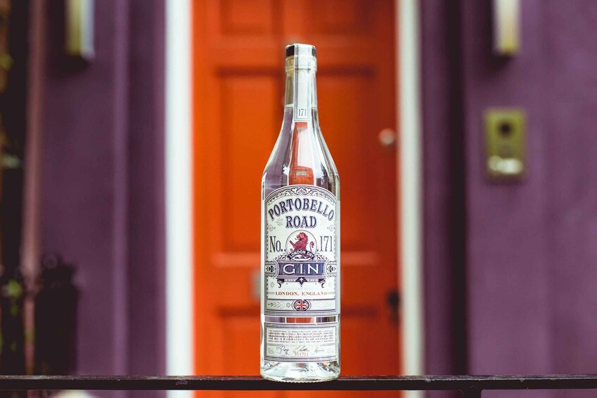 A bottle of Portobello Road Gin on a metal railing with a purple wall and an orange door in the background. 3