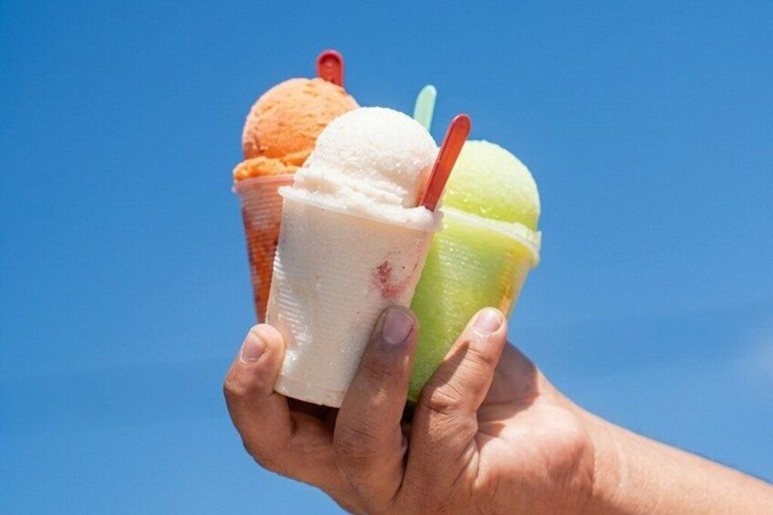 A hand holding three ice cream cones against a clear blue sky. 2