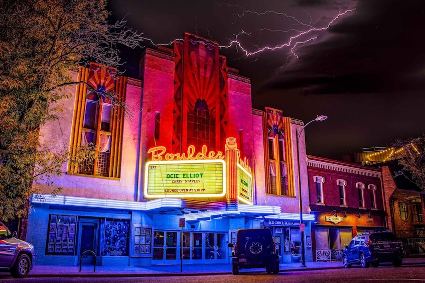 A theater with neon signs and a marquee advertising a show. 1