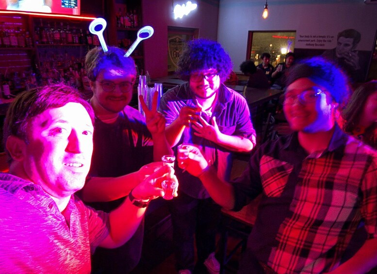 A group of people in a bar with neon lights and bottles in the background. 1