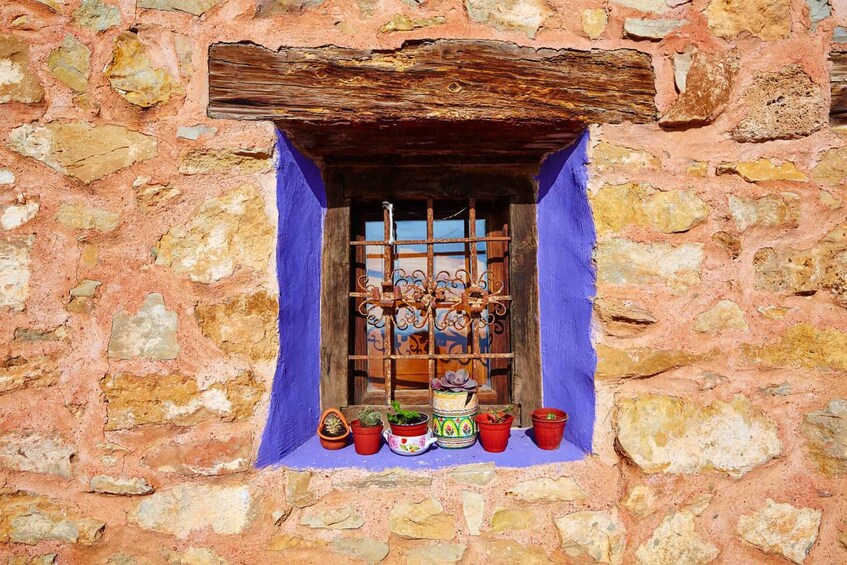 A stone wall with a window featuring a wooden shutter and a blue curtain. 4
