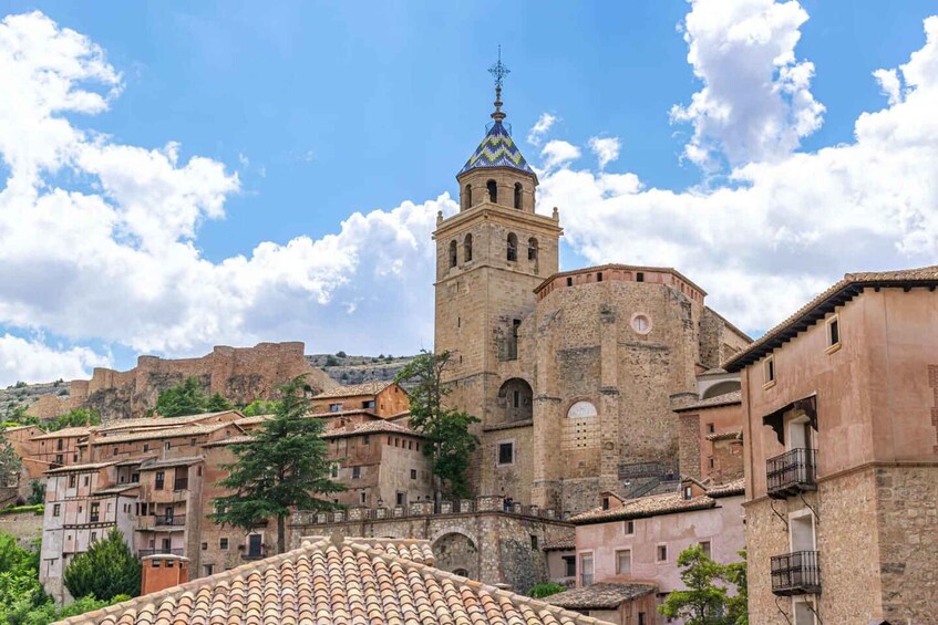 A historic town with a prominent tower, terracotta-roofed buildings, and a clear blue sky. 2