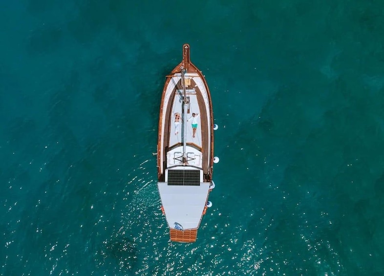 An aerial view of a boat with a white hull and a brown deck, floating on turquoise water. 1