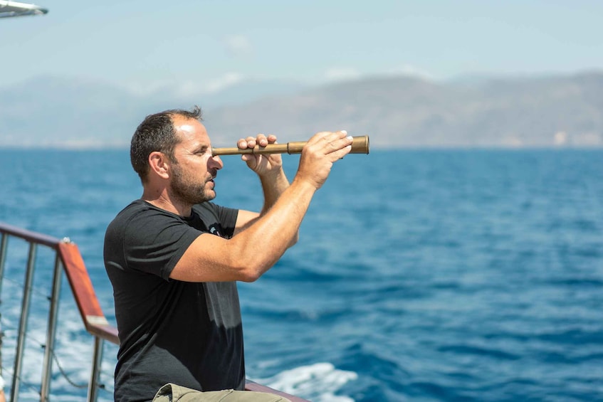 A person holding a brass telescope, looking out over a body of water with a distant landmass in the background. 3