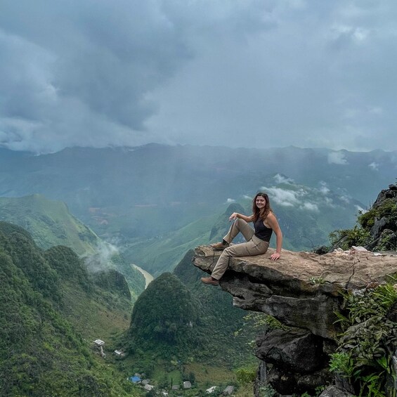 Une personne est assise sur un rebord rocheux, d’où elle a une vue sur une vallée avec des montagnes en arrière-plan. 5
