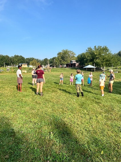 A group of people in a grassy field with a clear sky, some buildings, and trees in the background. 2