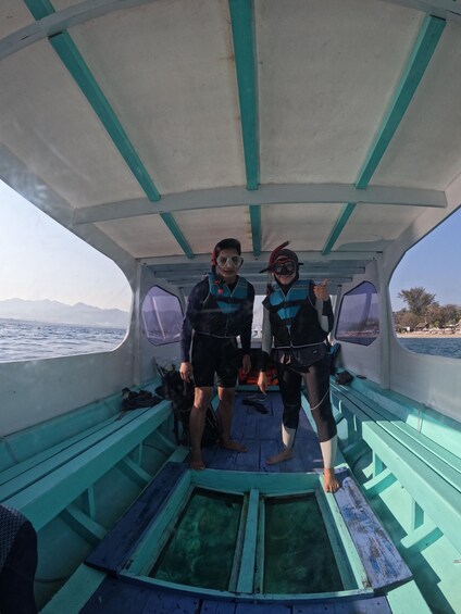 Zwei Personen mit Tauchausrüstung auf einem Boot mit Blick auf das Meer und die Berge. 4
