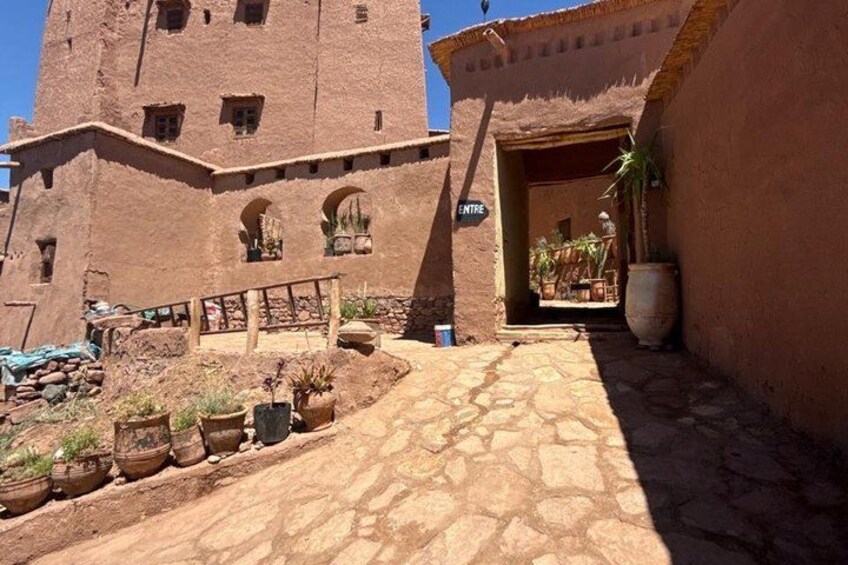 A rustic building with a tower, a paved pathway, and potted plants. 1