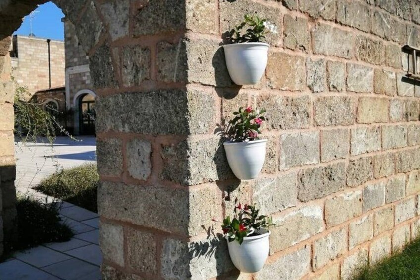 A stone wall with three white planters containing plants. 3