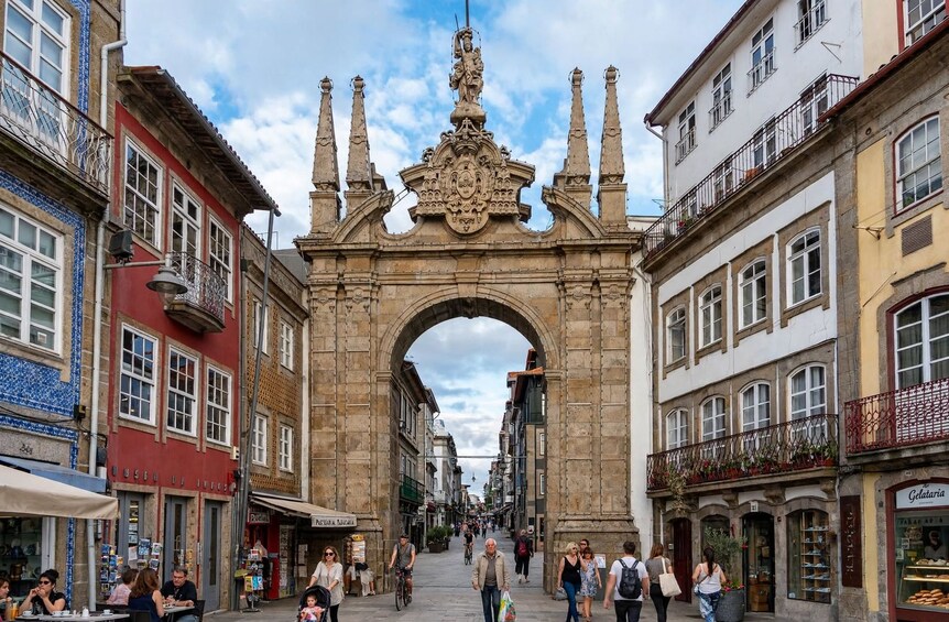 A historic archway in a bustling urban street with people walking and cycling. 1