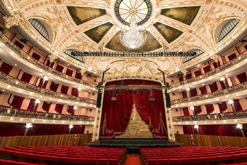 A grand theater with ornate gold detailing, red velvet curtains, and multiple balconies. 2