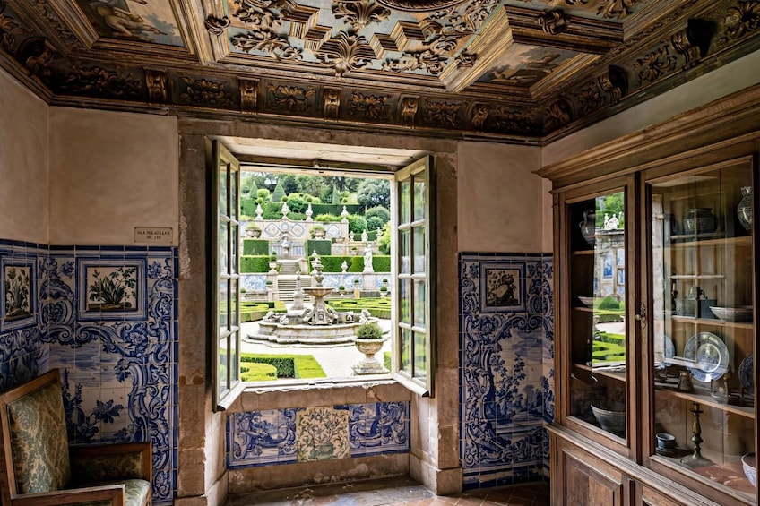 A room with ornate blue and white tiles, a window overlooking a garden, and a cabinet with glass doors. 4
