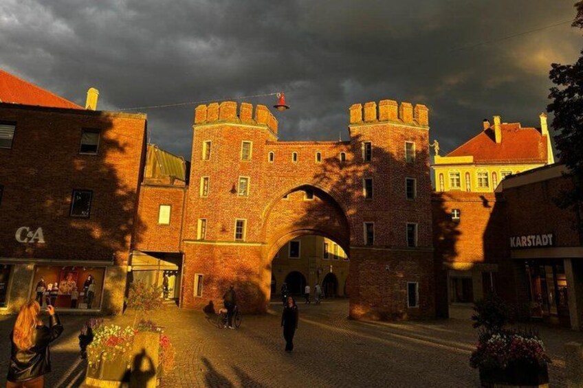 A historic brick building with a central archway, surrounded by modern buildings. 2