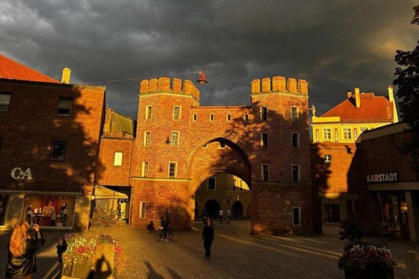 A historic brick building with a large archway, a flag, and a street with pedestrians. 2