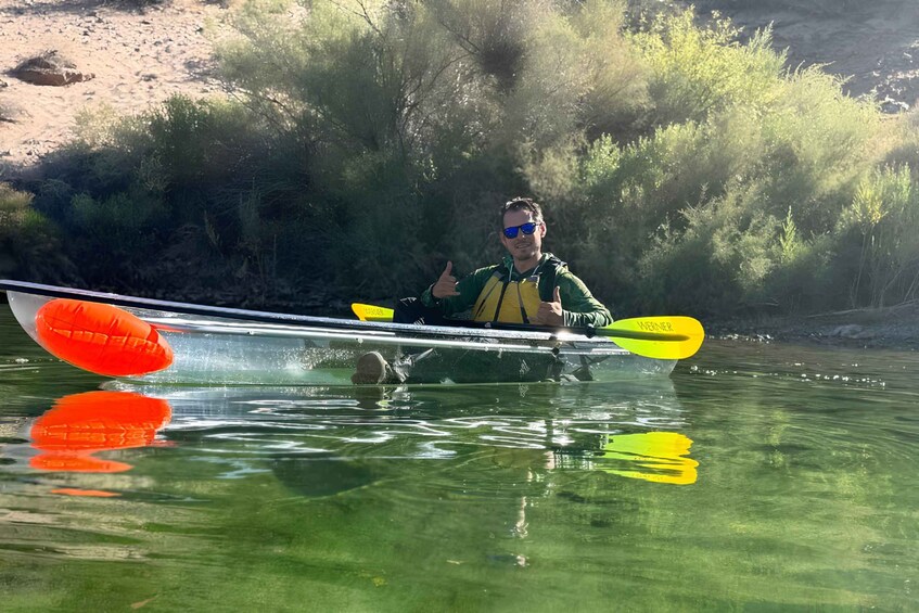 A person kayaking on a river with a clear view of the surrounding vegetation and a sandy bank in the background. 5