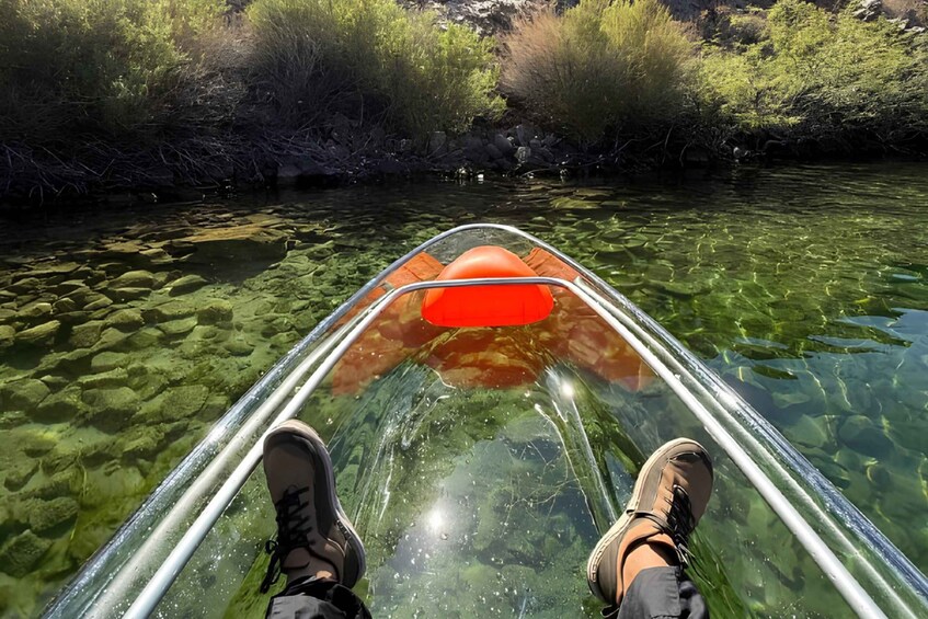 A person in a transparent kayak on a clear river with rocks and vegetation on the banks. 4