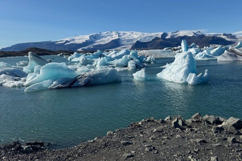 Icebergs in a body of water with a rocky shoreline and mountains in the background. 4
