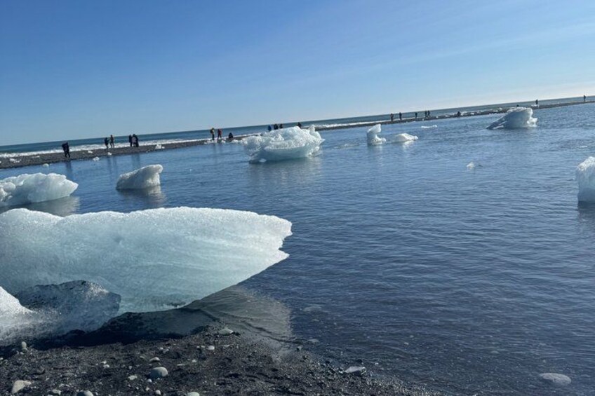 Icebergs floating in calm water, a clear sky, and a distant shoreline with people. 2