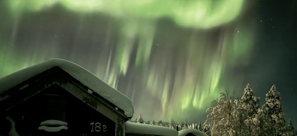 A snow-covered house with a number '18B' and a forest with snow-covered trees under the aurora borealis. 3