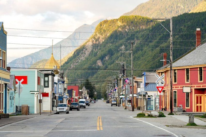 A street lined with colorful buildings, a railroad crossing, and mountains in the background. 5
