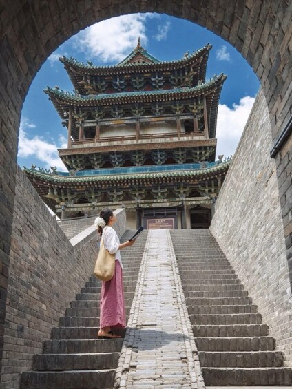 A person ascending a stone staircase towards a traditional multi-tiered building with ornate roof tiles. 2