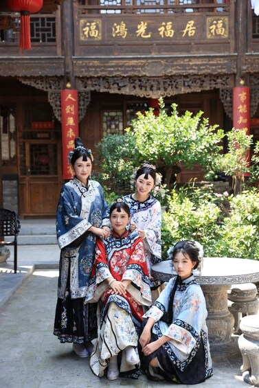 A group of people in traditional attire in front of a building with ornate architecture and a garden. 1