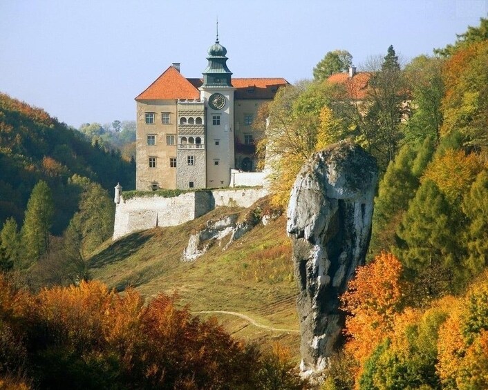 A castle on a hill with autumn foliage, a prominent rock formation, and a clear sky. 2