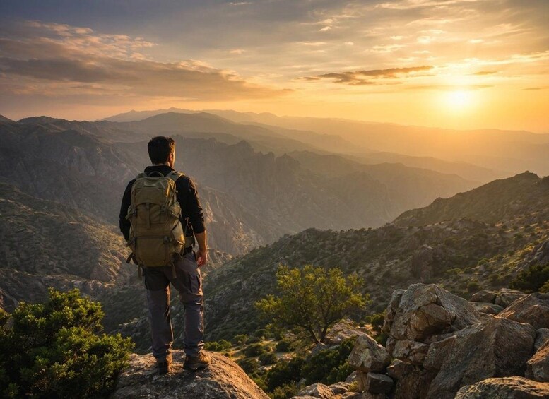 A hiker standing on a rocky outcrop overlooking a mountainous landscape during sunset. 1