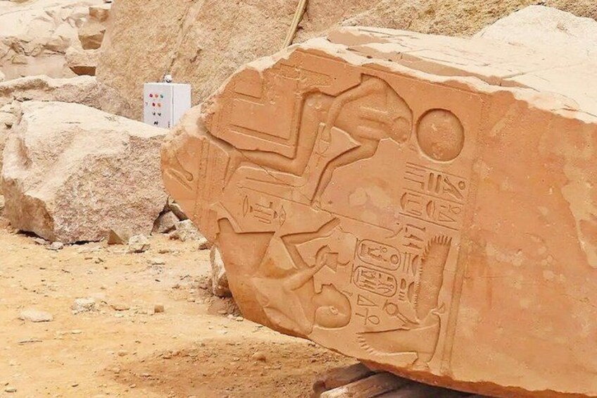 An ancient Egyptian sarcophagus with hieroglyphics, set against a desert backdrop with large rocks and a utility box. 5