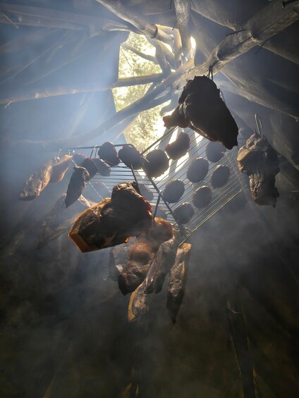 A meat roasting setup with skewers and a rack, surrounded by smoke. 4