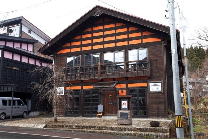 A traditional wooden building with a balcony, a small tree in front, and a parked car. 5