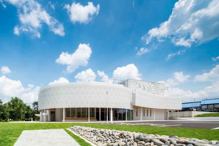A modern building with a curved facade and a landscaped area with rocks and grass in front. 3
