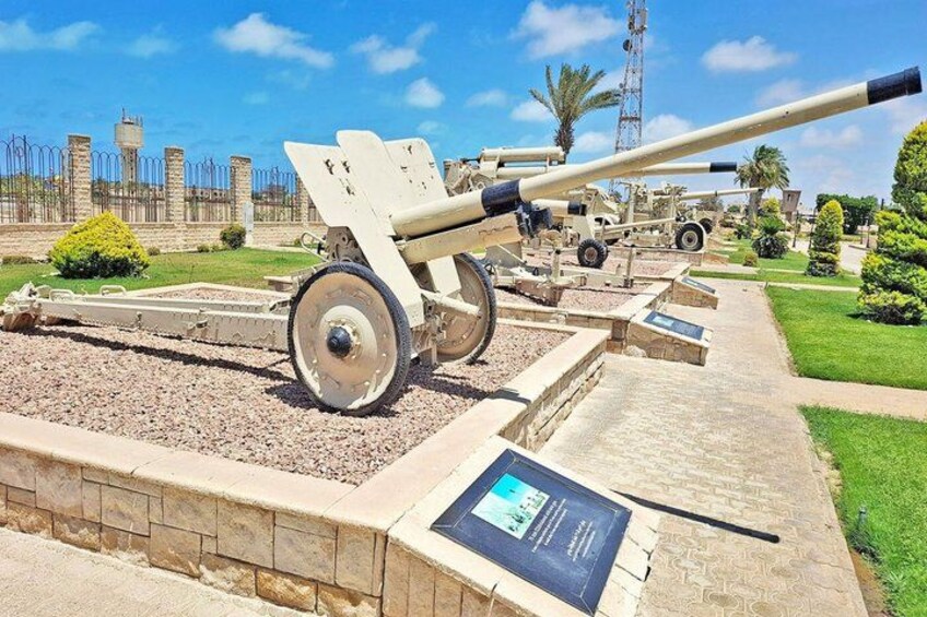 A cannon on display with a clear view of its barrel and wheels, set against a backdrop of a fence and greenery. 4