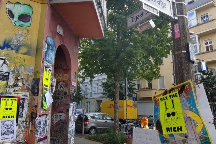 A street with graffiti-covered buildings, a tree, and street signs. 3