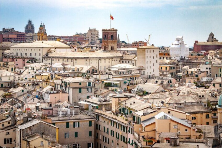 A densely packed urban area with historic buildings, a prominent church with a flag, and a large white structure in the distance. 2