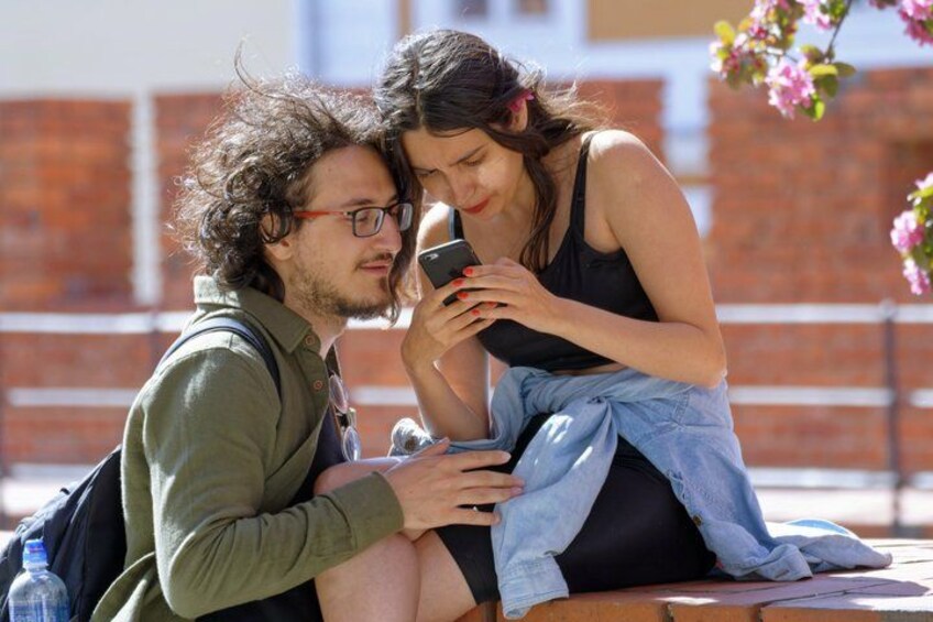 Two people sitting on a bench outdoors, one holding a smartphone. 1