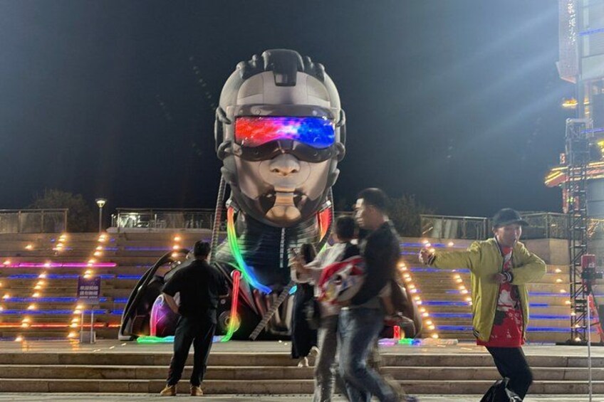 A large illuminated sculpture of a helmet with colorful lights, surrounded by steps and a crowd of people. 3